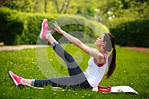 Sportive young woman stretching, doing fitness exercises in park