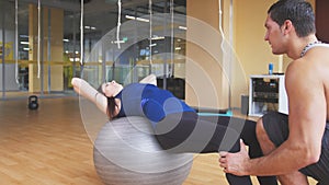 Sportive young woman with fitness instructor doing abdominal crunches on fitballs