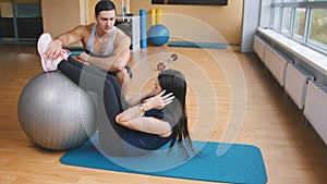 Sportive young woman with fitness instructor doing abdominal crunches on fitballs