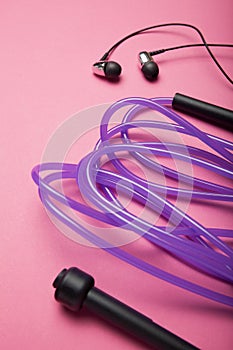 Sports accessories. Jump rope and headphones on a pink background