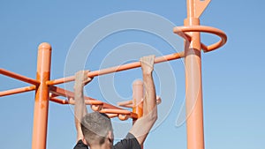 Sports activities on outdoor ground and healthy lifestyle. Athletic man doing pull ups on horizontal bar in city park. Fitness and