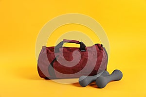 Sports bag and dumbbells on yellow background