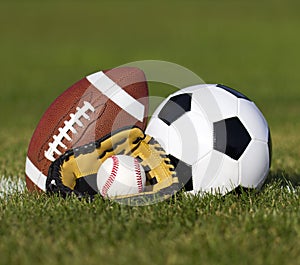 Sports balls on the field with yard line. Soccer ball, American football and Baseball in yellow glove on green grass