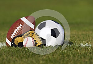 Sports balls on the field with yard line. Soccer ball, American football and Baseball in yellow glove on green grass