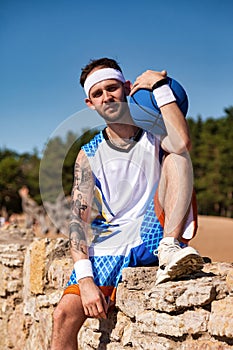 Sports and basketball concept. Sportsman with basketball ball in arm sitting in desert looking at camera smiling outdoors