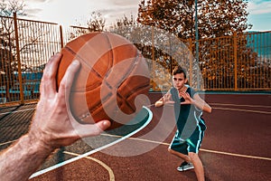 Sports and basketball. A man`s hand holds a basketball for submission. In the background, a teenager in a blur preparing to catch