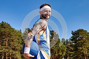 Sports and basketball. Young man with basketball in arm looking at camera smiling at blue sky outdoors