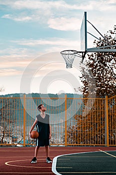 Sports and basketball. A young teenager in a black tracksuit stands on the Playground with a ball in his hands and looks defiantly