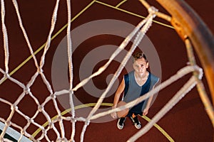 Sports and basketball. A young teenager in a blue tracksuit looks at a basketball basket. View from the basket