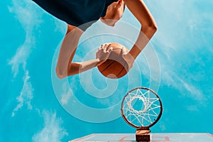 Sports and basketball. A young teenager in a blue tracksuit throws a ball into the basket. Bottom view. Blue sky in the background