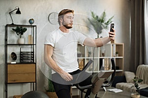 Sports bearded caucasian man in sportswear having online video call while cycling bike