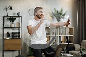 Sports bearded caucasian man in sportswear having online video call while cycling bike