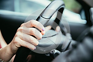 Sports car steering wheel, hands of a young girl with purple nail polish