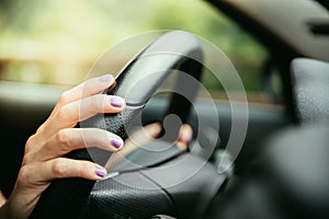 Sports car steering wheel, hands of a young girl with purple nail polish