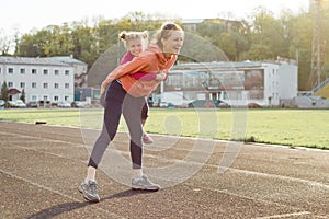 Sports cheerful family, healthy lifestyle, spring portrait of mother and little daughter having fun and running at the stadium