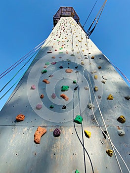 Sports climbing wall in perspective with various hooks, hanging rope belay. View from below