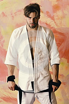 Sports and combat concept. Guy poses in white kimono holding black belt