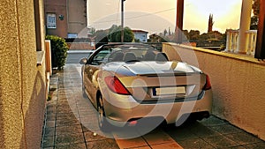 Sports convertible car parked in the driveway. Enjoyable cabriolet with top down against beautiful sunset light in the background