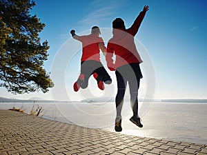 Sports couple crazy jumping on park path around frozen lake