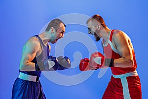 Sports emotions. Excited professional boxers in red and blue sports uniform boxing isolated on blue background in neon