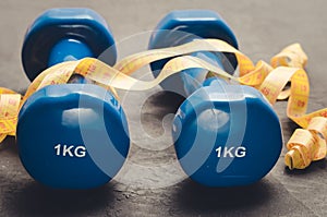 Sports equipment on a dark background/ Sports equipment with Blue dumbbells and yellow measuring tape. Selective focus