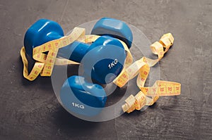 Sports equipment on a dark background. Top view/ Sports equipment with Blue dumbbells and yellow centimeter