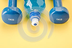 Sports equipment with dumbbells and bottle/blue dumbbells and bottle on a yellow background. Copy space. Top view