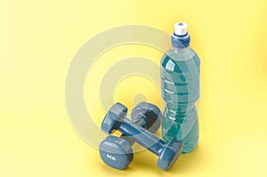 Sports equipment with dumbbells and bottle/blue dumbbells and bottle on a yellow background. selective focus. Copy space