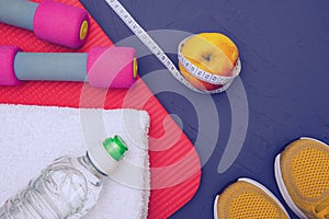 Sports equipment - mat, bottle of water and towel, sneakers, apple and measurement tape, lie on blue, textured background