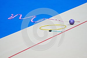 Sports equipment for rhythmic gymnastics lie on the edge of the carpet in the gym. Rhythmic gymnastics clubs, a ball, a hoop