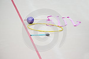 Sports equipment for rhythmic gymnastics lie on the edge of the carpet in the gym. Rhythmic gymnastics clubs, a ball, a hoop