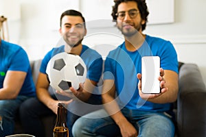 Sports fans texting and showing the smartphone while enjoying a soccer world cup on tv