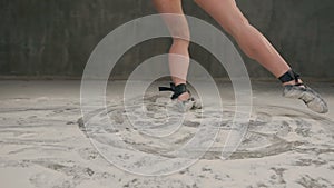 Sports female legs in pointe shoes perform modern dance and make circles of dust or flour that scattered on the floor in