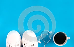 Sports flat lay with coffee, white sneakers and earphones on blue background. Fitness concept. Concept healthy lifestyle. Top view