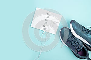 Sports flat layout. Fitness accessories sneakers, headphones and an open notebook for recording on a blue background