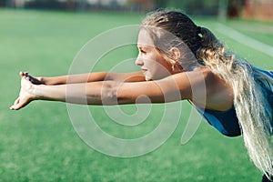 Sports girl in a blue shirt and leggings doing gymnastics workout on a football field. Fitness, sport, health energy. Close up.