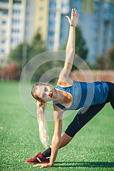 Sports girl doing in a blue shirt and leggings gymnastics workout on a football field. Fitness, sport, health energy.