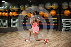 A sports girl doing leg exercises on a gym background. Fit young female with a fitness stick. Building muscles concept. photo