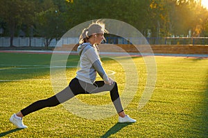 Sports girl doing morning gymnastics workout on green grass. In the control of warm sunlight. Fitness, sport, health, energy.