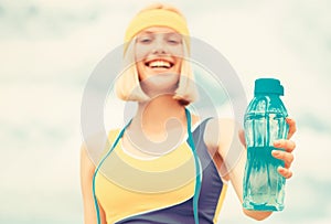 Sports girl drinks water from a bottle on a sky background. Drinking during sport. Woman in sportswear is holding a