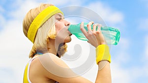 Sports girl drinks water from a bottle on a sky background. Healthy lifestyle concept. Drinking during sport. Young