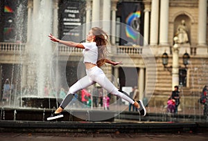 Sports girl gymnast jumping in flight on street of old city