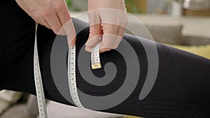 sports girl measures her body with tape measure. slender woman in tracksuit measures her thigh. concept of weight loss