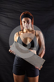 Sports girl in mud holds a blank sign in the studio on a black background