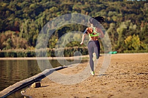 A sports girl runner runs along the shore of the lake jogging.