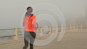 sports girl runs along the miami promenade in the fog with a bottle of water
