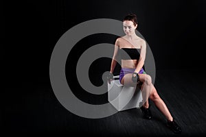 Sports girl sitting and looking at camera against black background.