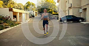 A sports girl in a sports summer uniform jogs along the yards on the street in the morning