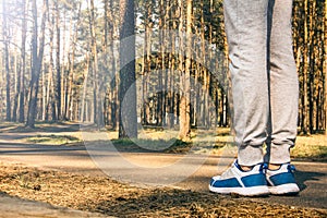A sports girl stands in the forest. Legs in sneakers close-up on a forest background