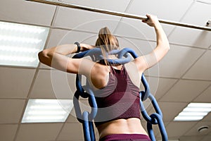 Sports girl with a weighting chain on her shoulders prepares for pull-ups